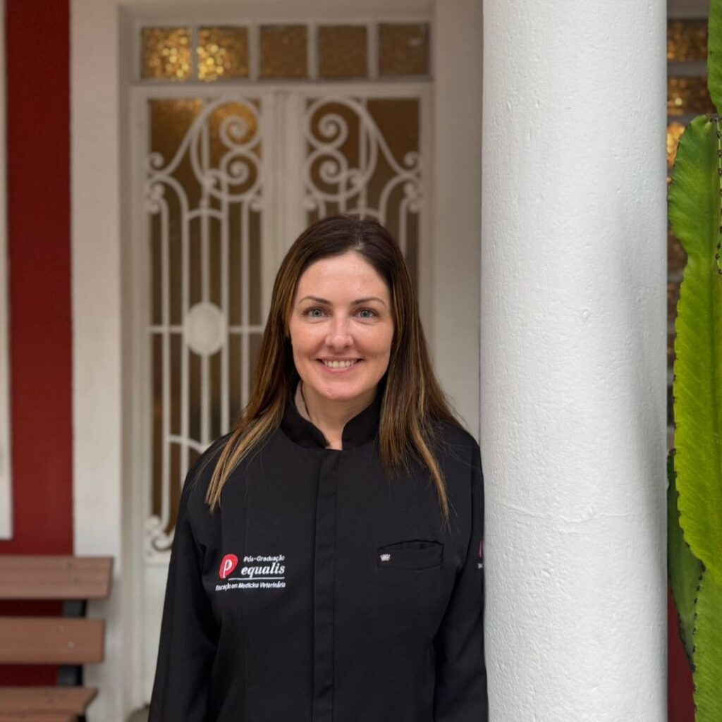 Smiling woman in a black uniform standing beside a white rounded column near a decorative wrought-iron gate.