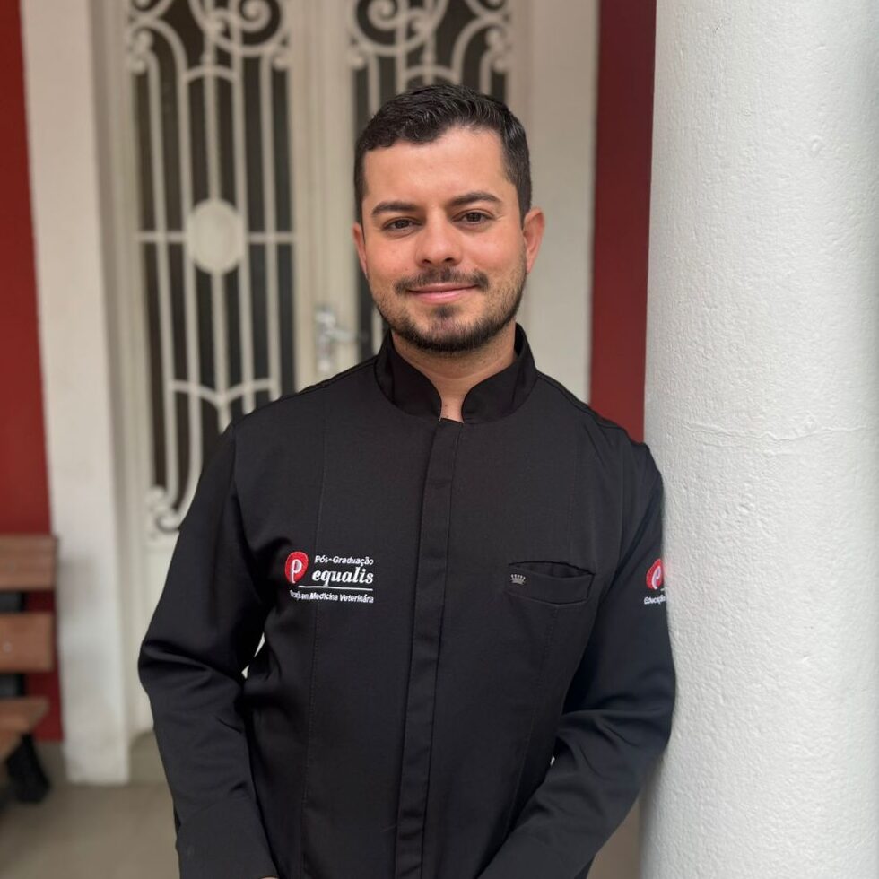 Man in a black chef jacket standing indoors in front of an ornate white door, smiling at the camera.